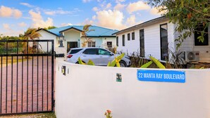 Un lotissement résidentiel fermé, avec une maison blanche, une voiture garée et un panneau indiquant « 22, boulevard Manta Ray ».