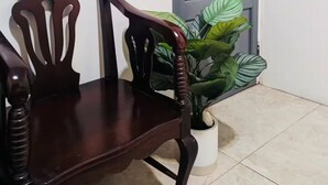 Un banc en bois doté d’un dossier incurvé et d’un accoudoir en bois, placé devant un mur blanc et une porte bleue.