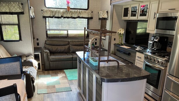 A compact RV kitchen with a central island, a dining area with a table and chairs, and a seating area with a sofa. - Charming 2-bedroom RV with WiFi and AC in peaceful Silverhill Alabama (Silverhill)