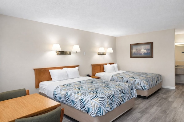 A hotel room with two beds, a desk, and a painting on the wall.