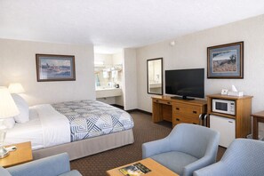 A hotel room with a bed, a desk with a television, a microwave, a chair, and a small table. - Sundowner Inn Forsyth I 94 (Forsyth)