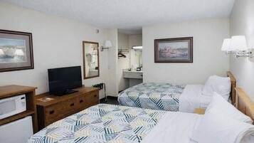Ein Hotelzimmer mit zwei Betten, einem Fernseher, einem Schreibtisch mit Mikrowelle und Bildern an den Wänden.