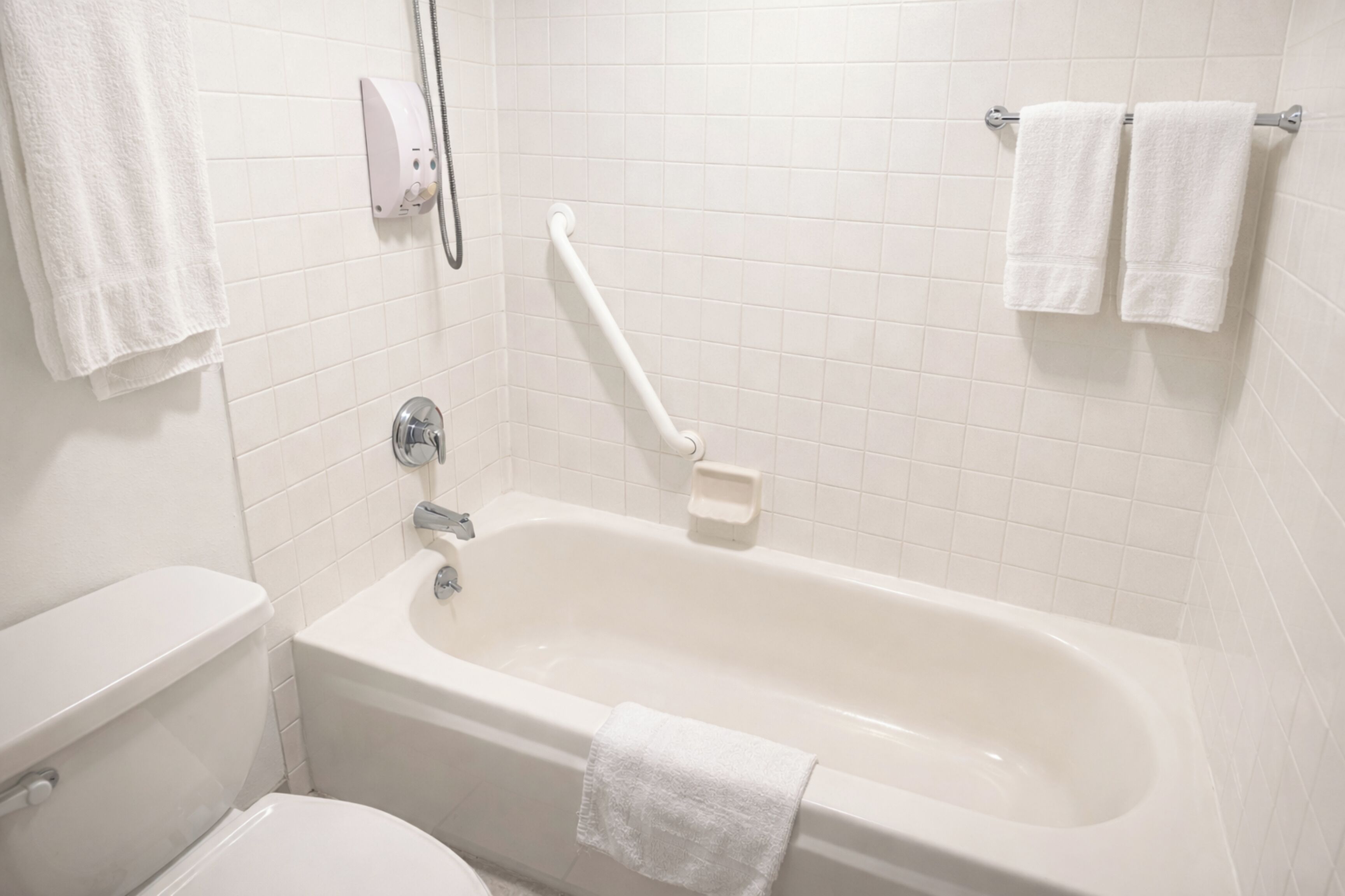 A bathroom with a bathtub, a toilet, and a handrail.