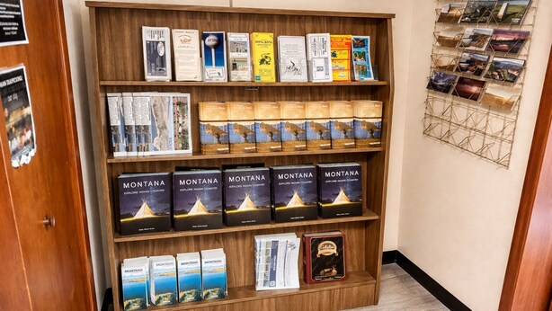 Una estantería de madera con varias guías de viaje y mapas, incluyendo múltiples ejemplares de 'Montana Explore Indian Country'.