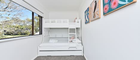 A bunk bed room with a window, carpeted floor, and two framed artworks on the wall.