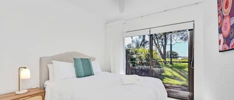 Een slaapkamer met een bed, bedlampje en uitzicht op groen via een schuifdeur.