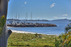 A marina with boats docked, a rocky breakwater, and a grassy area with a bench.