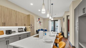 Une cuisine moderne dotée d’un grand îlot central, de meubles en bois et d’un coin repas avec des chaises orange.