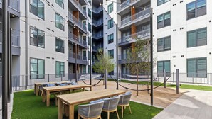 Un immeuble d’appartements moderne doté de nombreux balcons, d’un espace extérieur aménagé avec des tables et des chaises, et d’un petit arbre.