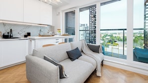 A modern apartment with a sofa, a dining area, and large windows offering city views. - Apartament Tower by Kairos Apartments (Katowice)
