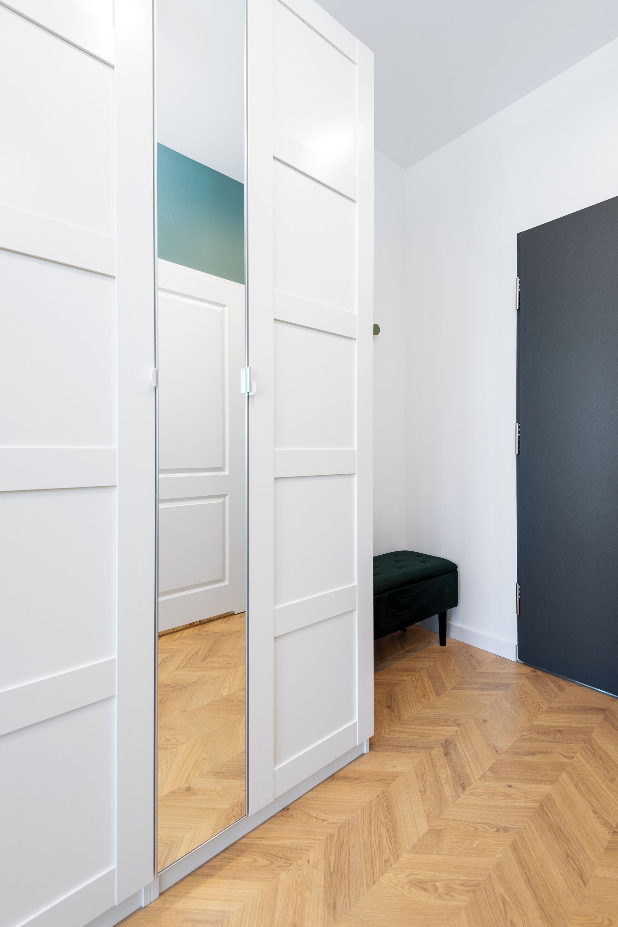 Een kamer met een houten visgraatvloer, witte muren en een donkere deur.