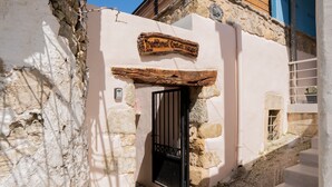 A traditional stone house with a wooden sign above the entrance, a black gate, and a stone staircase leading up. - Traditional Cretan House (Faistos)