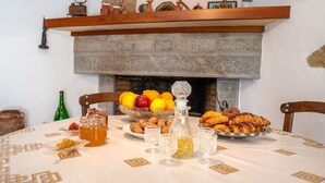 A dining table set with fruits, pastries, and drinks, with a fireplace in the background. - Traditional Cretan House (Faistos)