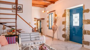A cozy living room with a staircase, a blue door, stone walls, and a sofa with patterned cushions. - Traditional Cretan House (Faistos)