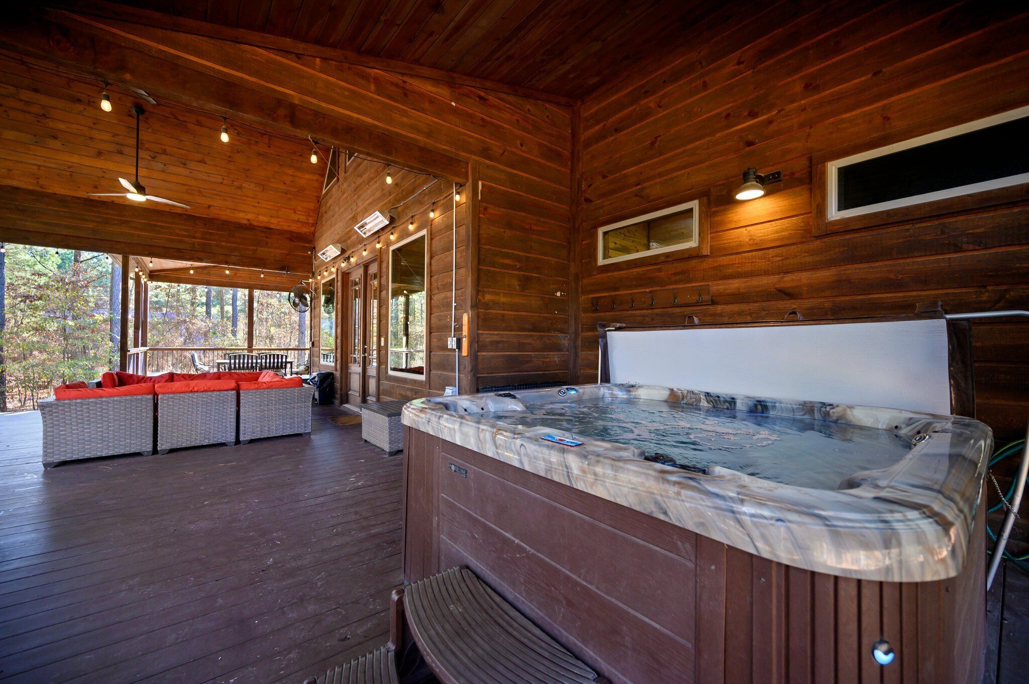Een houten hut met een jacuzzi, buitenzitplaatsen en een overdekt terras.