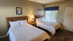Een hotelkamer met twee bedden, een plafondventilator, een raam met jaloezieën en een deur.