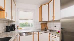 Una cocina con armarios blancos, un lavamanos de acero inoxidable, una cafetera y un refrigerador.