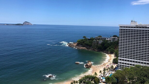 Un hotel frente al mar con vista a la playa y una isla distante.
