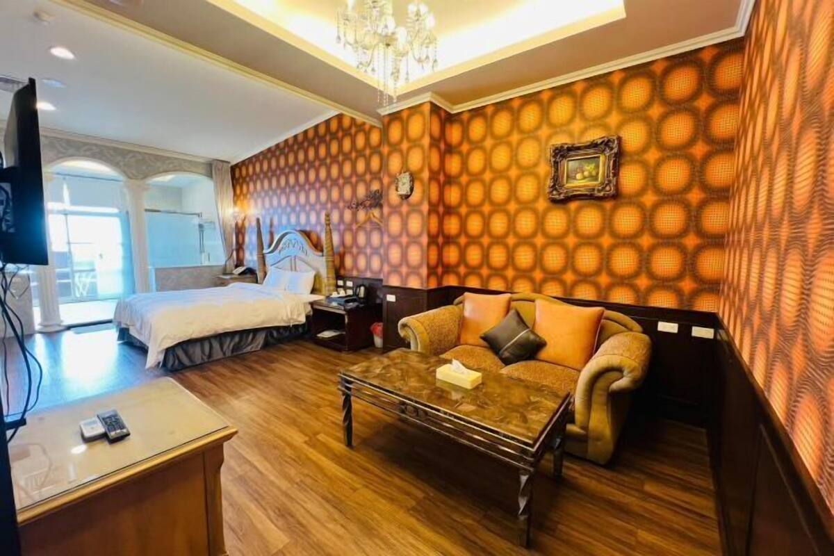 Habitación de hotel con cama, sofá, mesa de centro, televisión y un papel tapiz estampado.