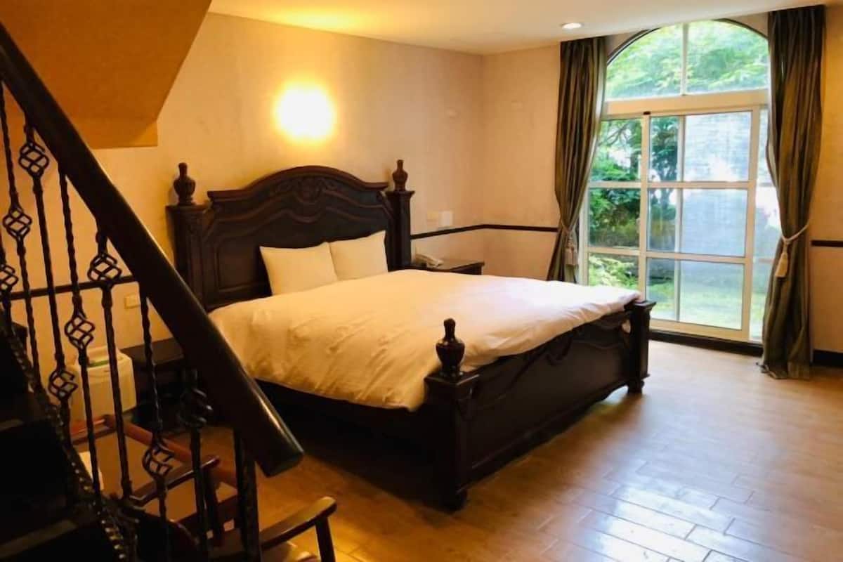 Un dormitorio con una cama grande, cabecera de madera, una ventana con cortinas y una escalera con barandilla.