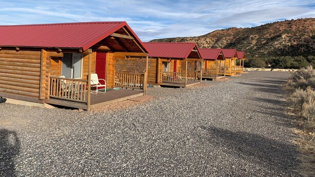 A row of log cabins with red roofs and wooden porches, set against a hilly backdrop.