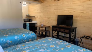 Una habitación con dos camas, televisión, una pequeña kitchenette y paredes de madera.