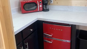 A compact kitchen with a red refrigerator, a microwave, and a coffee maker on the countertop.