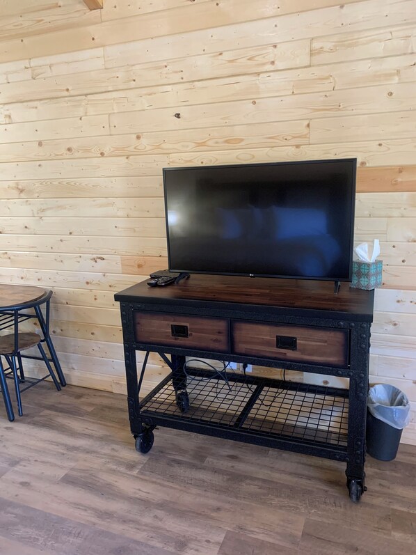 A wooden wall with a TV on a dark wooden desk with drawers, a chair, and a trash can.