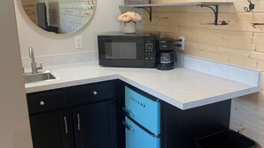 A compact kitchen with a sink, a black microwave, a coffee maker, and a blue dishwasher.