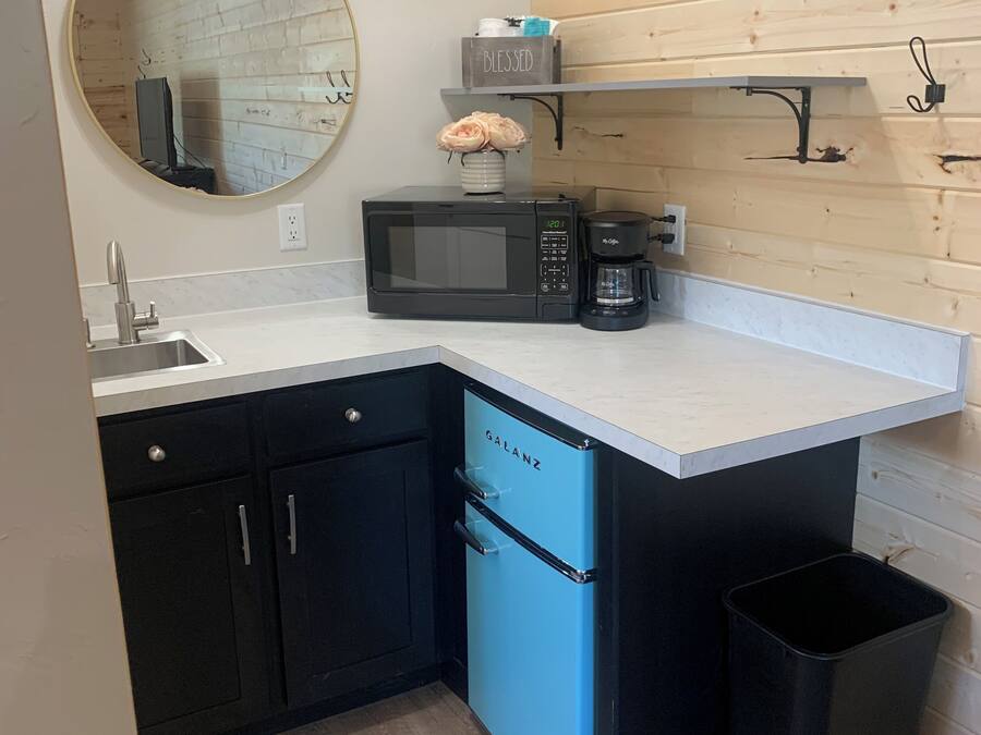 A compact kitchen with a sink, a black microwave, a coffee maker, and a blue dishwasher.