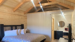 A wooden-paneled bedroom with a bed, bedside table, and a small kitchenette.