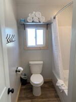 Un baño pequeño con inodoro, ventana, cortina de ducha y repisa con toallas.