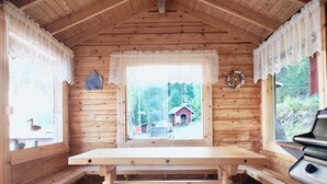 Una cabaña de madera con una mesa grande, bancos y una vista a un edificio rojo en la distancia.