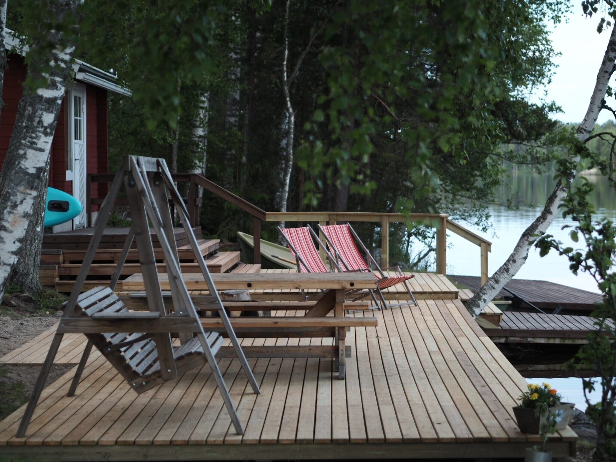 A wooden deck with a swing set, a small building, and a row of red and white striped lounge chairs.