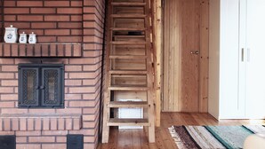 Una escalera de madera conduce a un dormitorio tipo loft con chimenea de ladrillo, armarios de madera y un armario blanco.