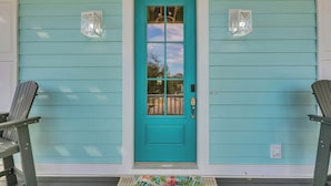 Une porte turquoise avec un panneau de verre, deux lanternes fixées au mur et un paillasson orné de motifs floraux.
