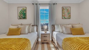Une chambre d’hôtel avec deux lits, une fenêtre avec des rideaux et des œuvres d’art accrochées aux murs.