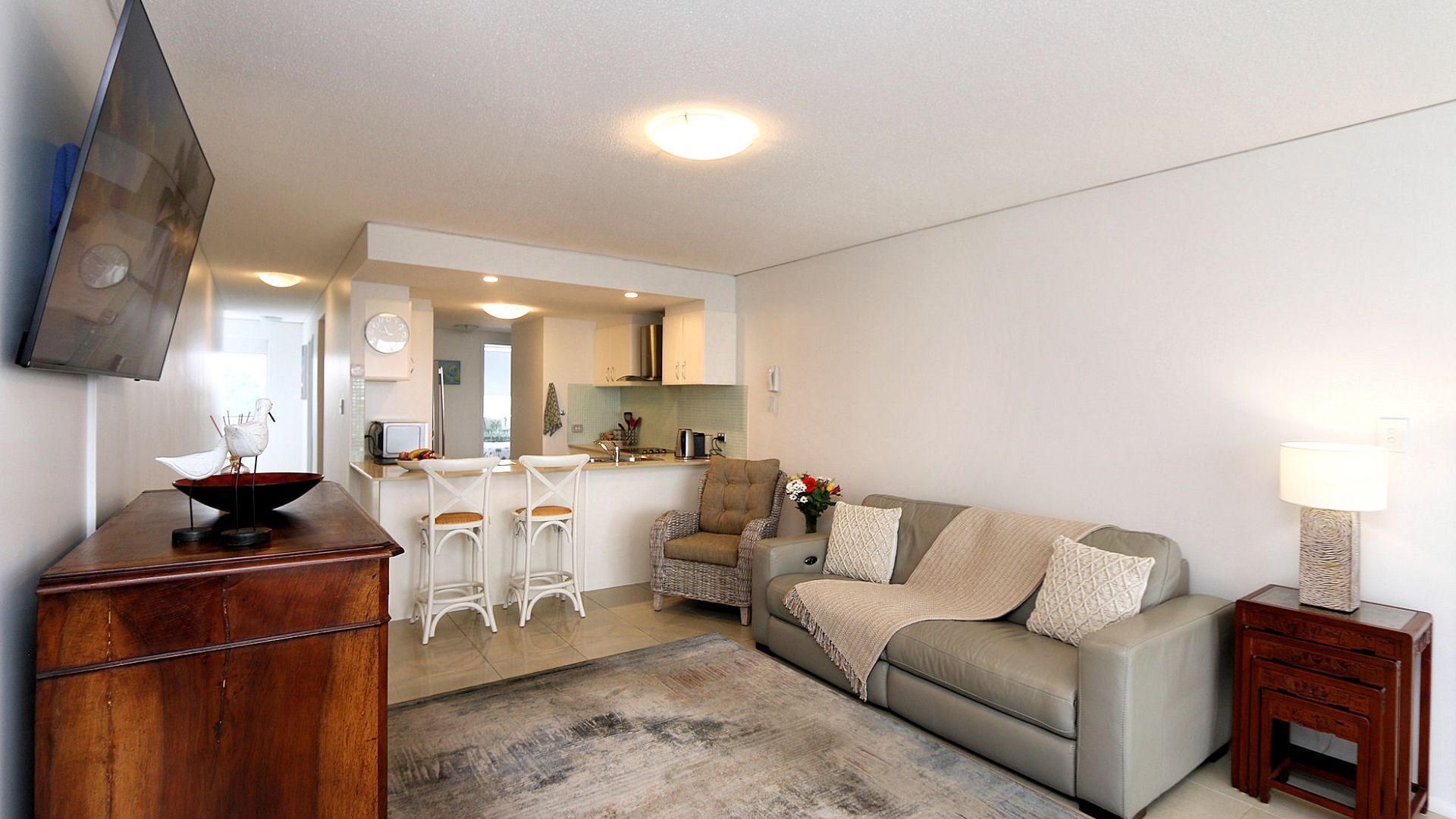 Een moderne woonkamer met een bank, een salontafel, een televisie en een keuken op de achtergrond.