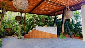 A covered outdoor area with a wooden slatted roof, a concrete bench, and hanging wicker baskets. - Meraki Luxury Condo by Marea  (Tulum)