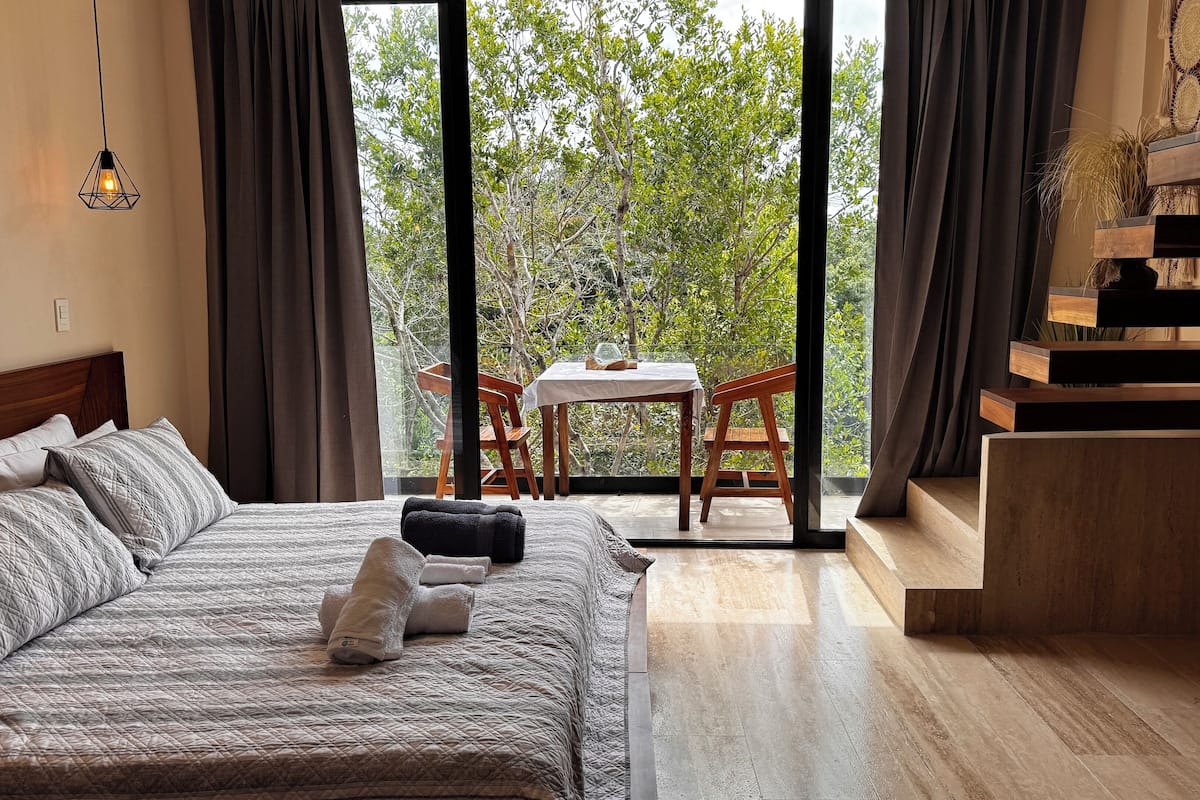 A bedroom with a large bed, a wooden headboard, a nightstand, and a view of the outdoors through a sliding door.
