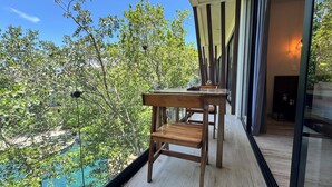 A balcony with a wooden table and chairs overlooking a swimming pool and lush greenery. - Meraki Luxury Condo by Marea  (Tulum)