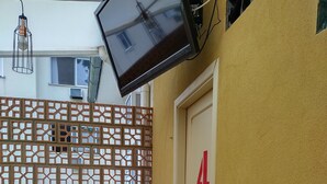 A room with a door marked '4', a TV mounted on the wall, a potted plant, and a wooden chair. - Soul Hostel 2 (Sao Paulo)