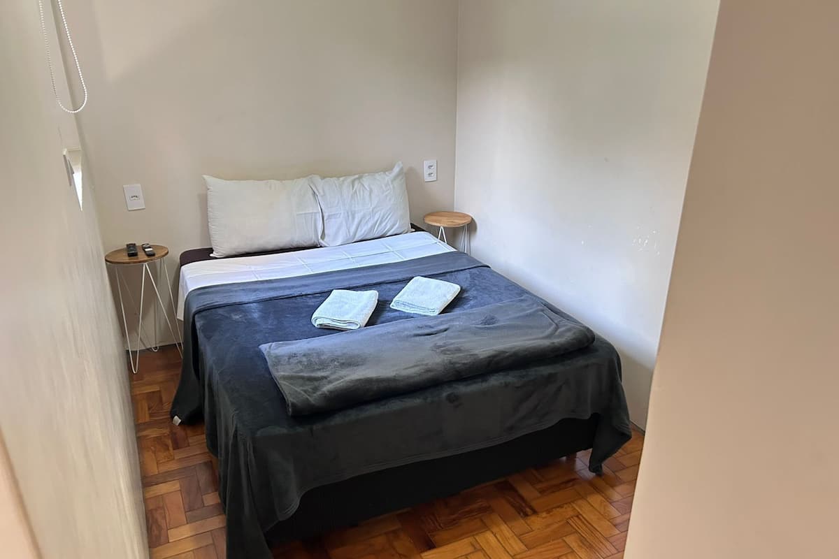 Ein kleines, ordentlich eingerichtetes Schlafzimmer mit einem Bett, Nachttischen und Holzboden.