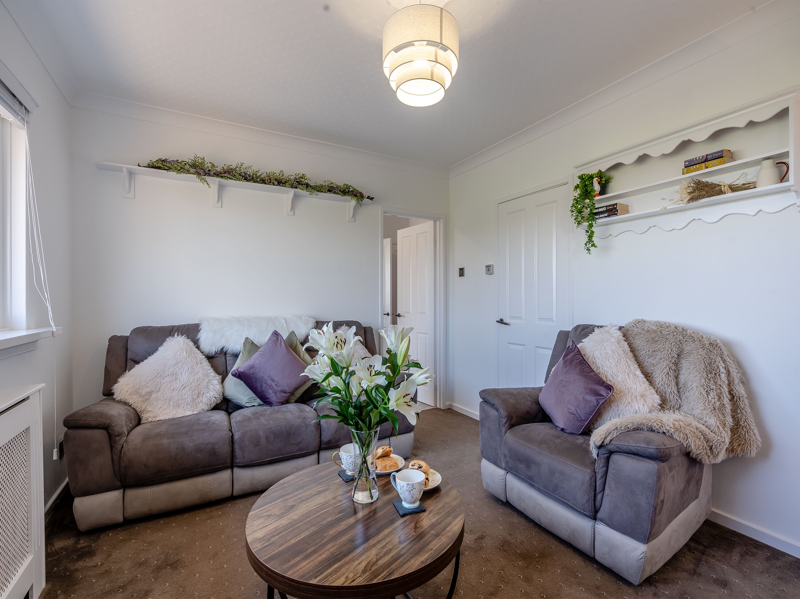 Un saló amb dos sofàs grisos, una taula baixa de fusta i un ram d'un vas de flors blanques.