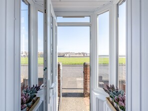 An open door leading to a paved area with a grassy field and buildings in the distance. - 2 bedroom accommodation in Berwick Upon Tweed (Berwick Upon Tweed)