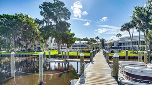 A wooden dock leading to a marina with boats, surrounded by trees and a building with large windows. - St Johns River Retreat in Welaka w/ Dock Access (Welaka)