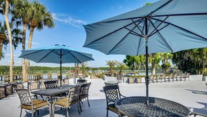 Outdoor seating with umbrellas, tables, and chairs, overlooking a body of water and palm trees. - St Johns River Retreat in Welaka w/ Dock Access (Welaka)