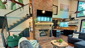 A modern living room with a brick fireplace, a staircase, and a kitchen area. - 9 bdrm covered dock, firepit and large bar on water, Baltic hot tub, sleeps 26, (lafollette)
