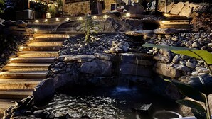 A stone staircase leading to a pool area with a waterfall, surrounded by rocks and plants. - 9 bdrm covered dock, firepit and large bar on water, Baltic hot tub, sleeps 26, (lafollette)