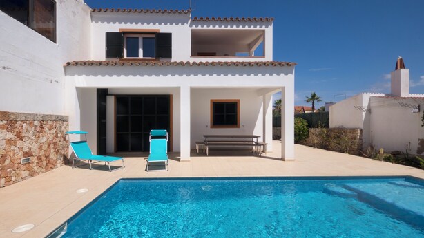 A two-story house with a swimming pool, a patio with lounge chairs, and a stone wall. - Llevant 11 E1 (Cap d'Artrutx)